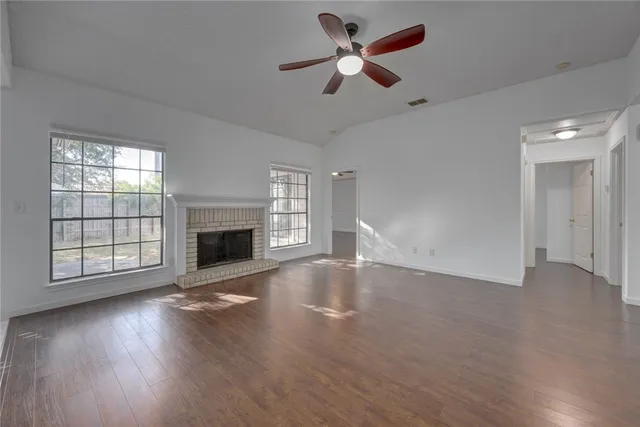 an empty room with windows fireplace and a ceiling fan