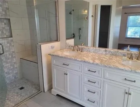 a bathroom with a granite countertop sink two mirror and shower