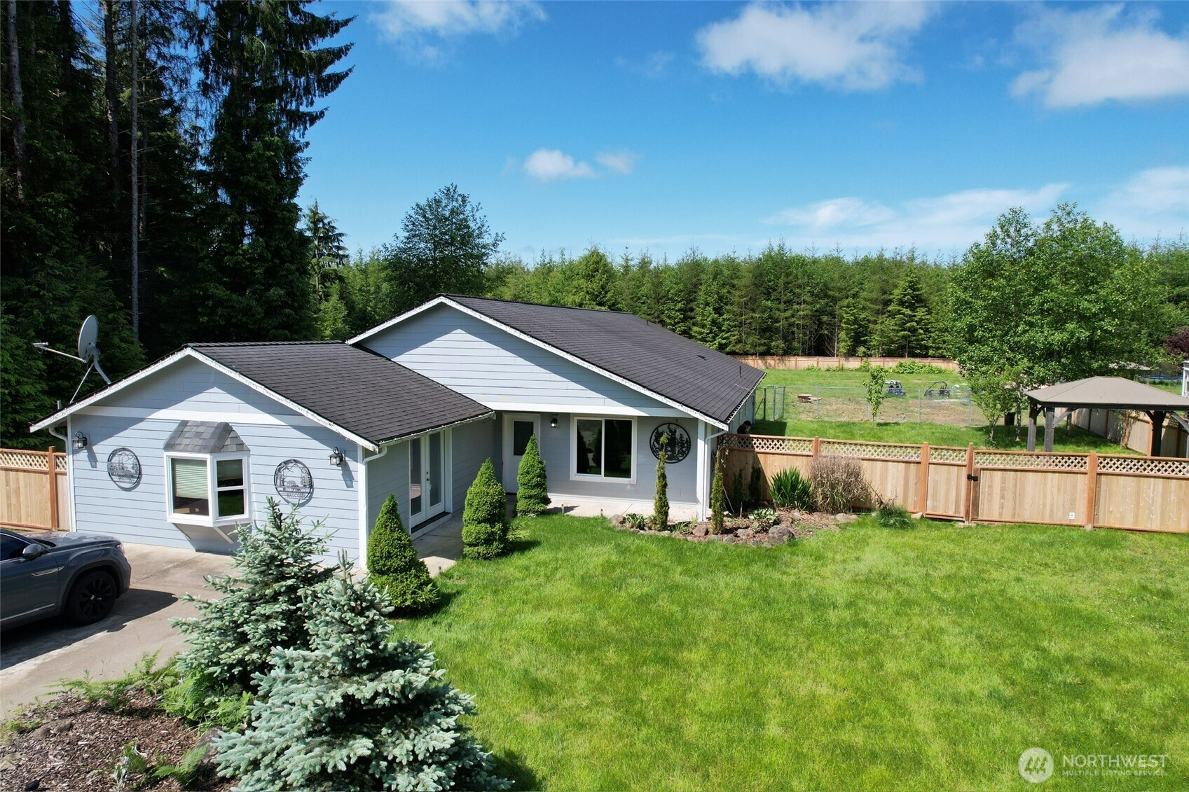 a house that is sitting in the grass with large trees and plants