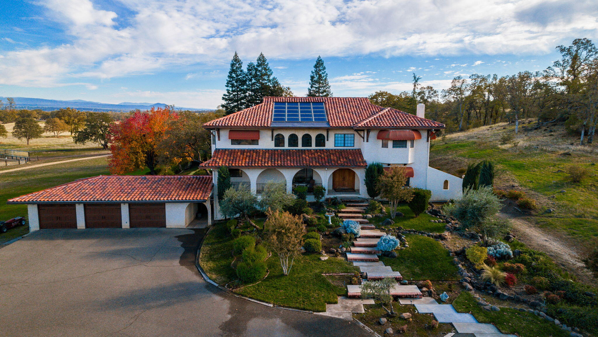 a view of a big house in front of a big yard with plants and large trees