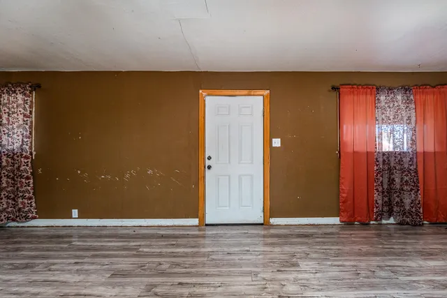 an empty room with wooden floor and windows with curtains