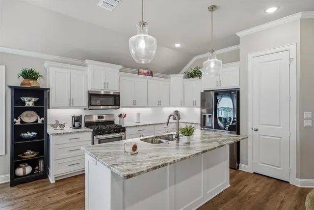 a kitchen with stainless steel appliances kitchen island granite countertop a sink dishwasher a refrigerator and a stove with wooden floor