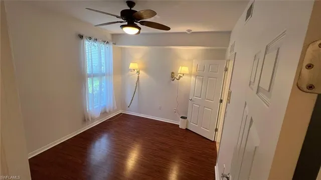 a view of an empty room with wooden floor and a ceiling fan