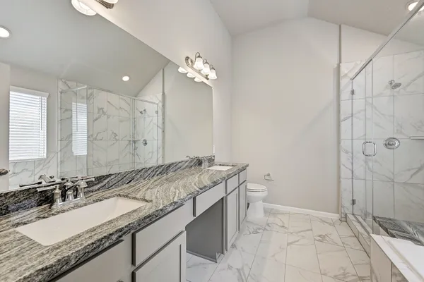 a bathroom with a granite countertop sink a toilet a mirror and shower