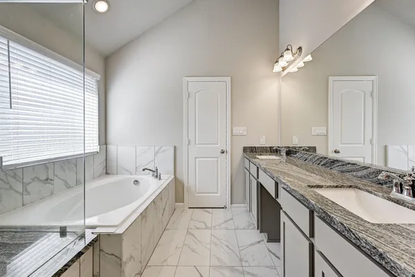 a spacious bathroom with a granite countertop sink a bathtub a mirror and vanity