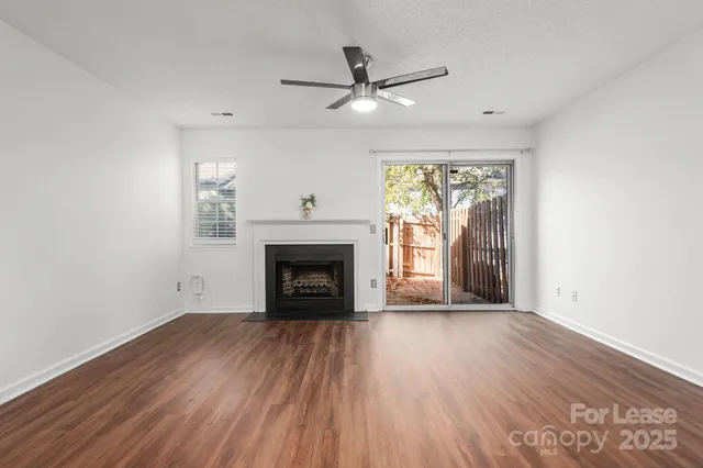 a view of an empty room with wooden floor fireplace and a window