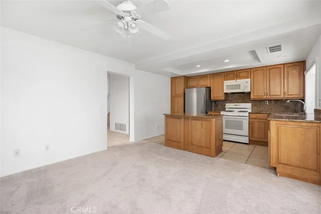 a kitchen with granite countertop a refrigerator oven a sink dishwasher and white cabinets with wooden floor