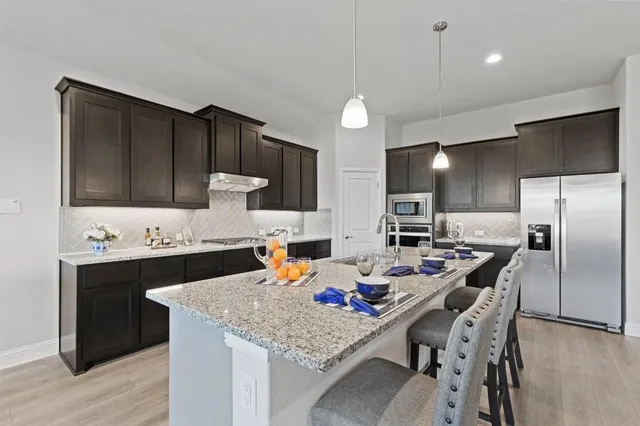 a kitchen with stainless steel appliances a microwave a stove a refrigerator a sink dishwasher a dining table and chairs with wooden floor