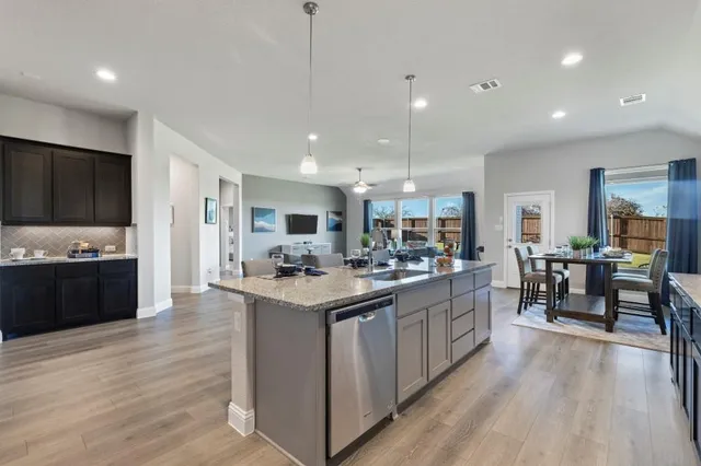 a kitchen with stainless steel appliances kitchen island granite countertop a dining table chairs refrigerator microwave and cabinets
