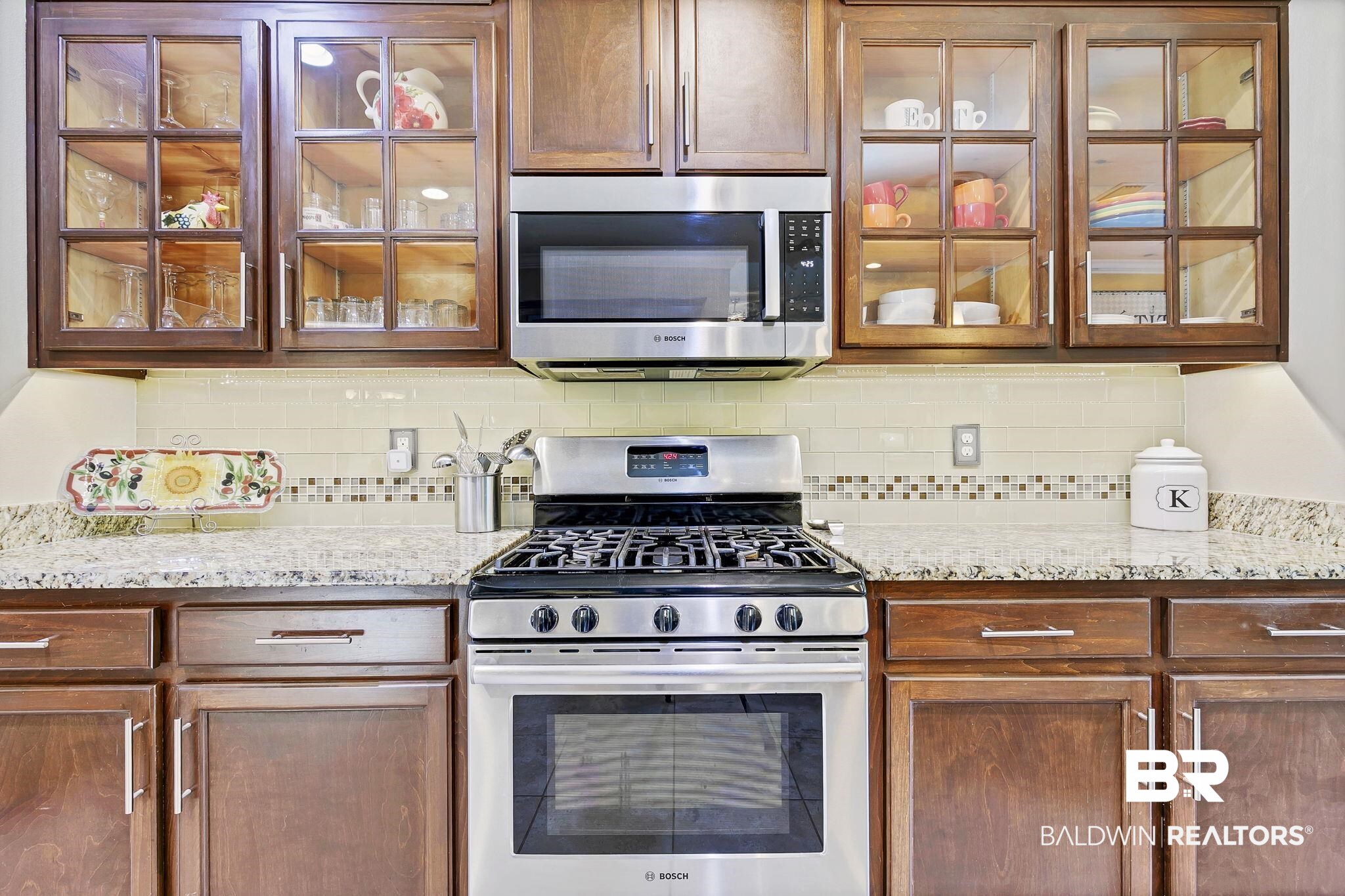 20105 Bunker Loop Fairhope, AL 36532 - Photo 21 of 65 Kitchen with decorative backsplash, light stone counters, glass insert cabinets, and appliances with stainless steel finishes