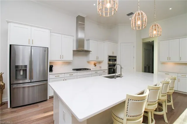 a kitchen with stainless steel appliances a refrigerator a stove a sink dishwasher a dining table and chairs with wooden floor