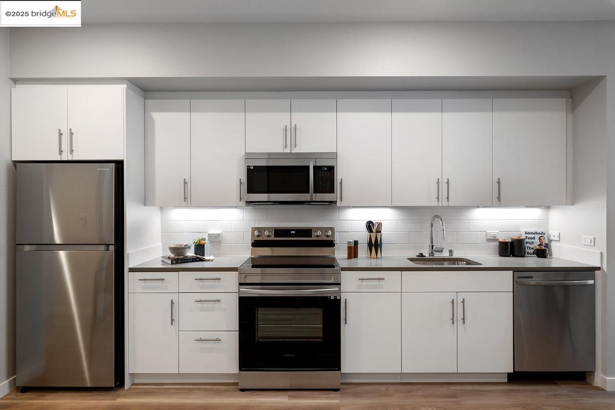 260 Brooklyn Basin Way, Unit 428 Oakland, CA 94606 - Photo 13 of 44 Kitchen with stainless steel appliances, white cabinetry, tasteful backsplash, and light wood finished floors