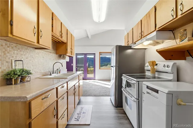 a kitchen with stainless steel appliances granite countertop a refrigerator a stove and a sink with wooden floors