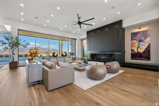 2867 East Granite Way St. George, UT 84790 - Photo 4 of 69 Living area with full-height glass walls showcasing mountain and desert scenery, a linear fireplace with a dark stone surround, wood-finish flooring, a contemporary ceiling fan, and recessed lighting