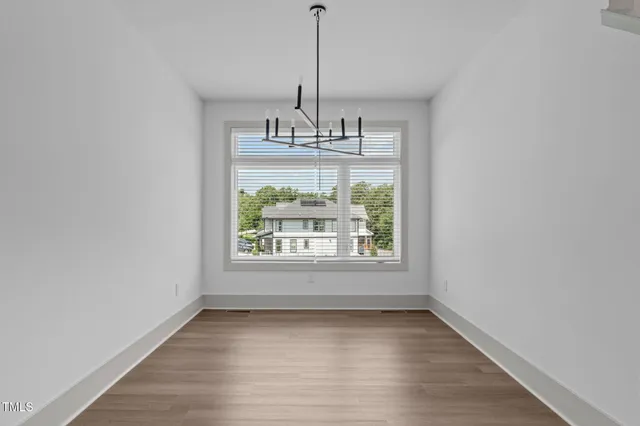 an empty room with wooden floor chandelier and window
