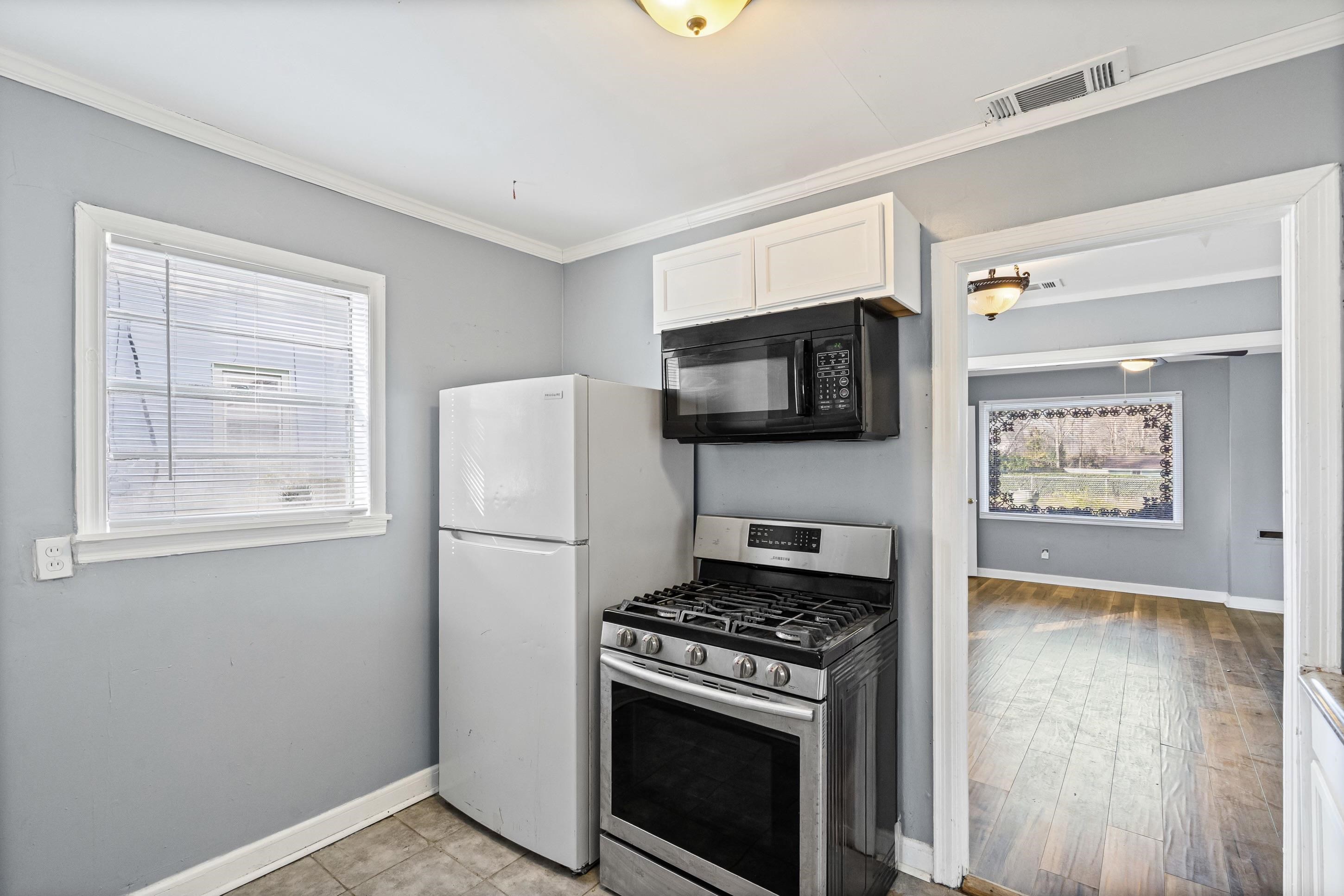 1848 Wynton Street Memphis, TN 38106 - Photo 10 of 22 Kitchen with gas stove, black microwave, ornamental molding, white cabinets, and freestanding refrigerator