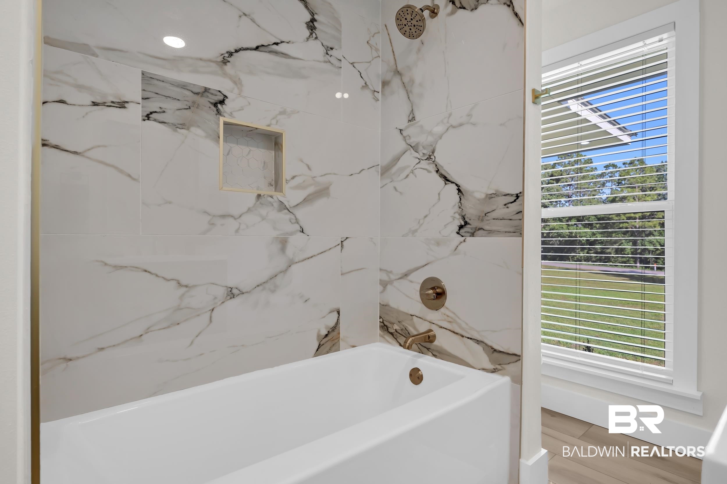 8170 Wilmer Georgetown Road Wilmer, AL 36587 - Photo 22 of 31 Bathtub with a large-format white and black veined tile surround, featuring a built-in shower niche with gold-toned trim