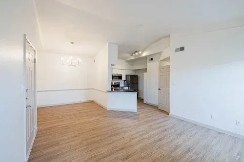 an empty room with wooden floor and a kitchen