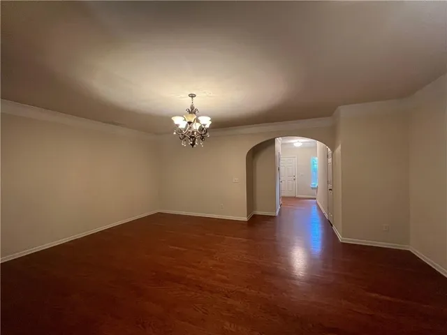 an empty room with wooden floor chandelier and windows
