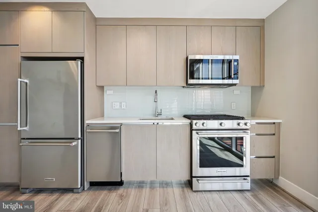 a view of an empty room with wooden floor and a kitchen