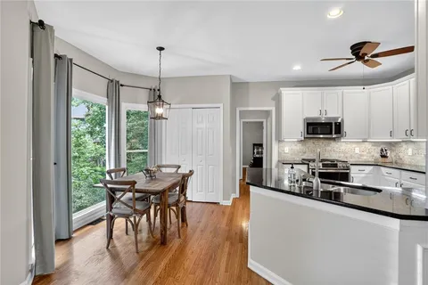 a kitchen with stainless steel appliances granite countertop a stove a refrigerator a microwave a dining table and chairs with wooden floor