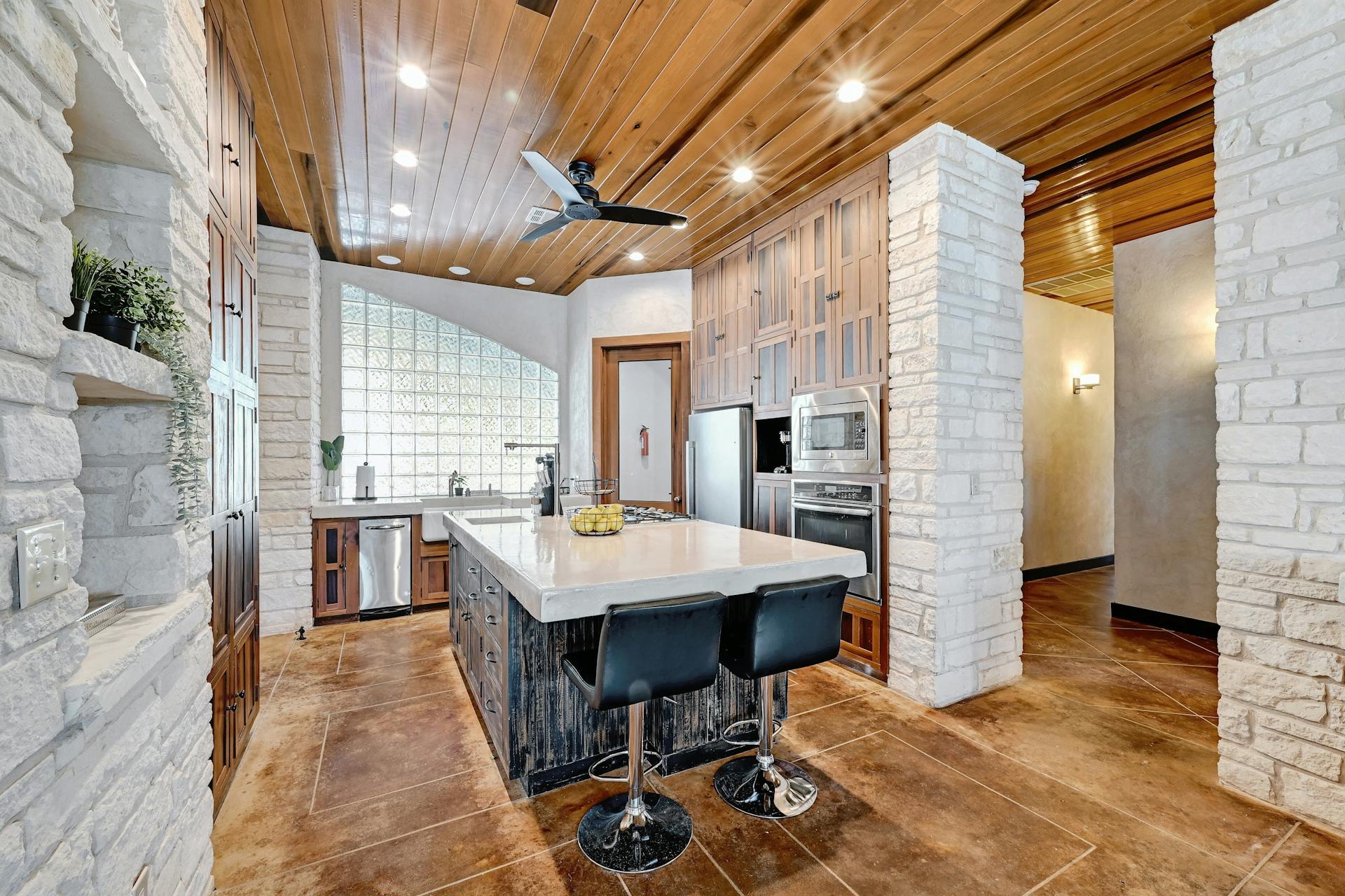 6021 Circle J Road Marble Falls, TX 78654 - Photo 27 of 39 Two tone kitchen featuring wood ceiling, a center island with sink, a kitchen bar, stainless steel appliances, and glass fronted cabinets