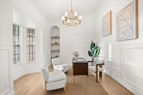 a view of a white house in front of a big yard plants and large trees