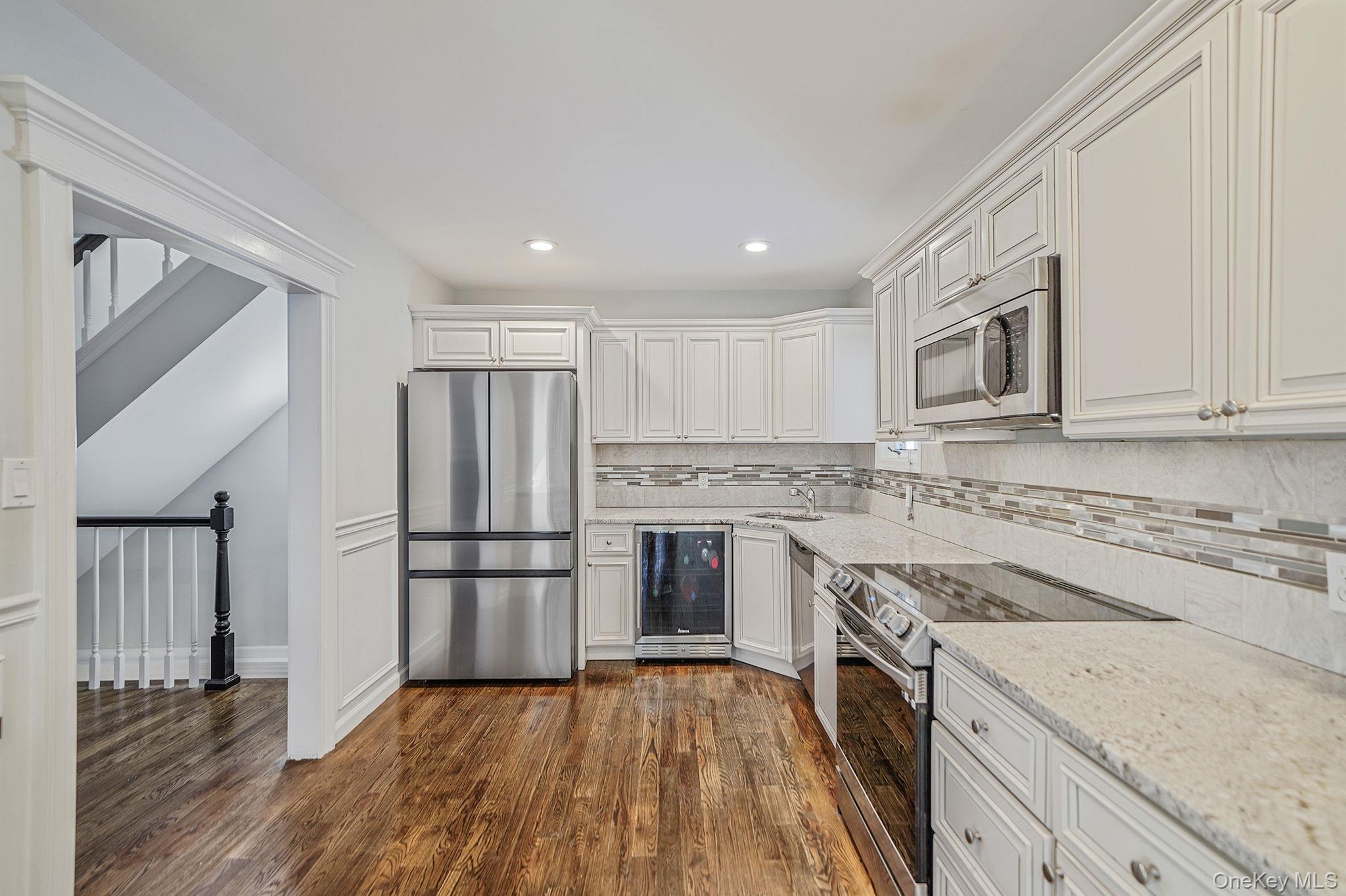 38 Hawthorne Road Rocky Point, NY 11778 - Photo 11 of 30 Kitchen featuring stainless steel appliances, beverage cooler, white cabinetry, light stone counters, and dark wood-style flooring