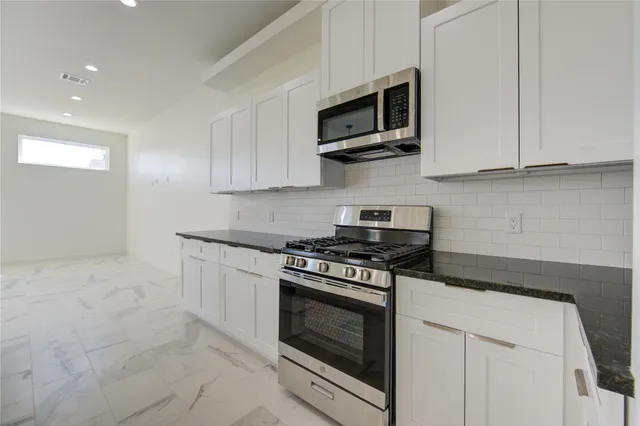 a kitchen with stainless steel appliances granite countertop grey cabinets a stove a sink and a microwave