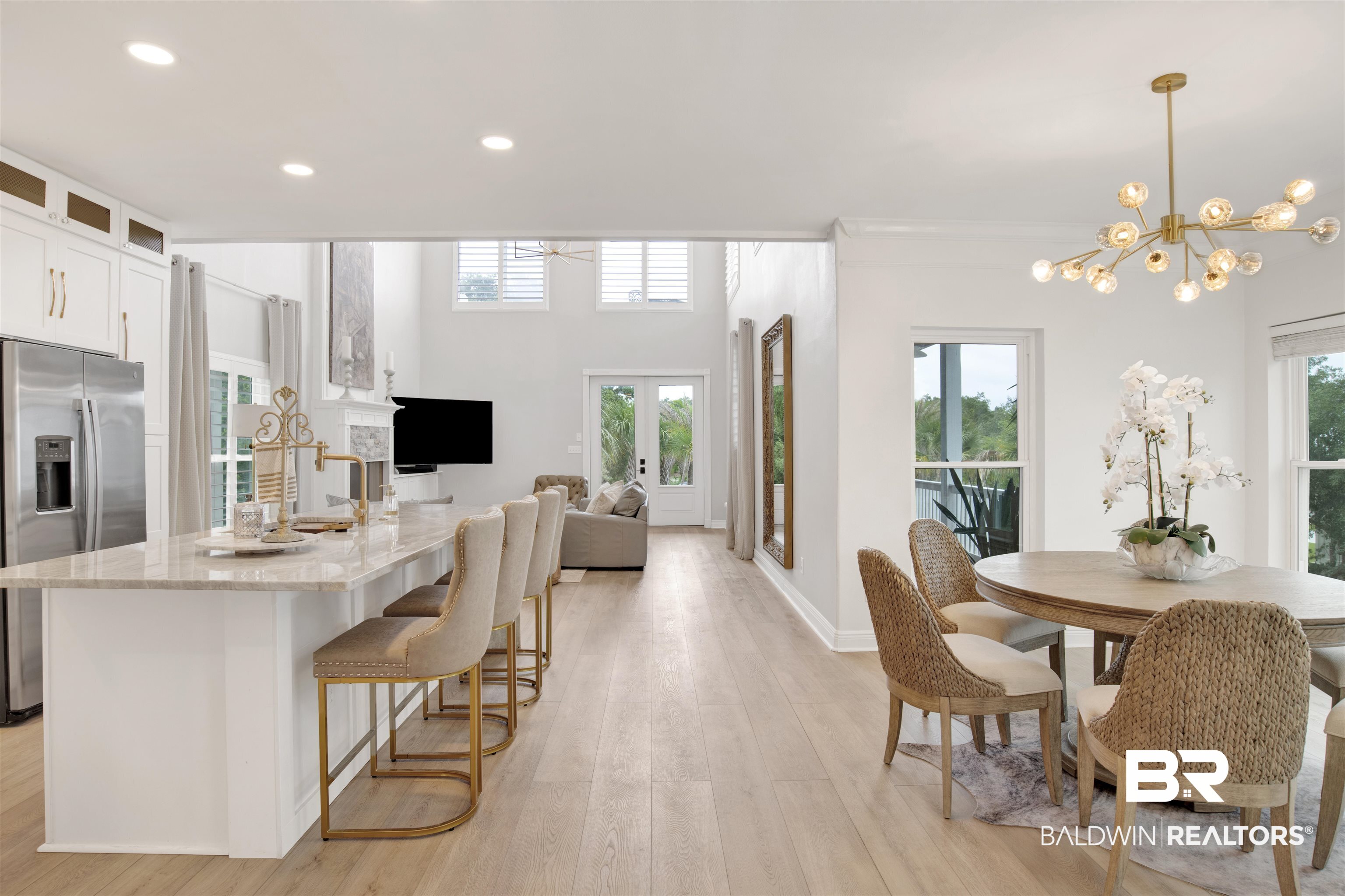 30351 River Road Orange Beach, AL 36561 - Photo 11 of 44 Open-concept living space featuring light wood-finish flooring, a kitchen island with a light-toned countertop, white cabinetry with gold-toned hardware, and a modern gold-toned chandelier