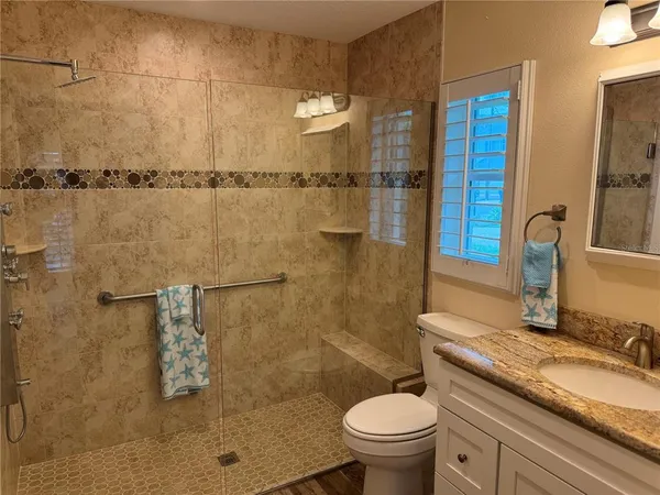 a bathroom with a granite countertop sink a toilet a mirror and shower