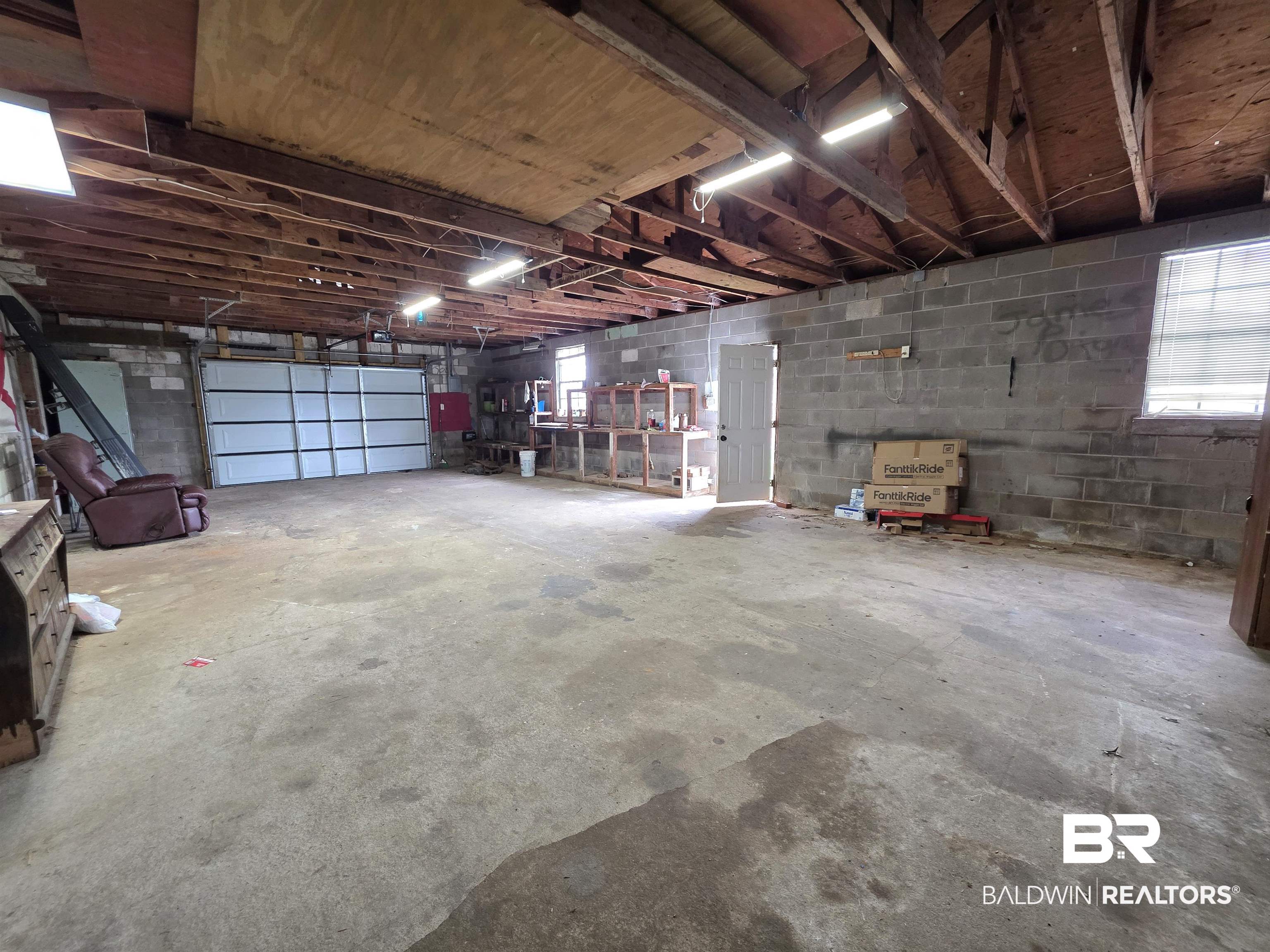 558 Stanton Road Atmore, AL 36502 - Photo 27 of 29 Spacious garage area featuring a concrete floor, exposed wood ceiling joists, overhead strip lighting, a white panel garage door, and block wall construction