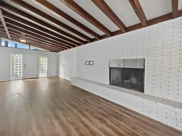 a view of an empty room with wooden floor and a fireplace