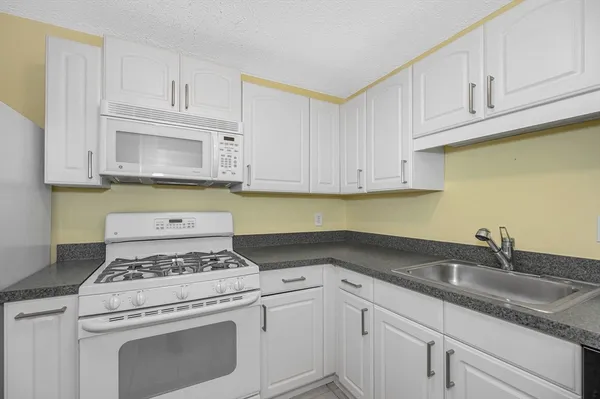 a kitchen with granite countertop white cabinets and a stove a sink
