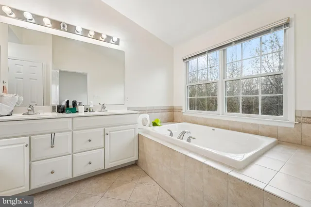 a spacious bathroom with a tub a double vanity sink a window and a mirror