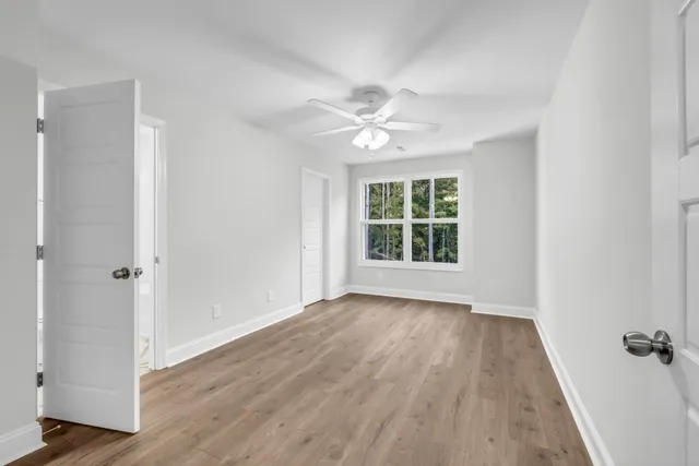 an empty room with wooden floor fan and windows