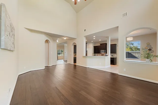 a view of an empty room with wooden floor and a kitchen