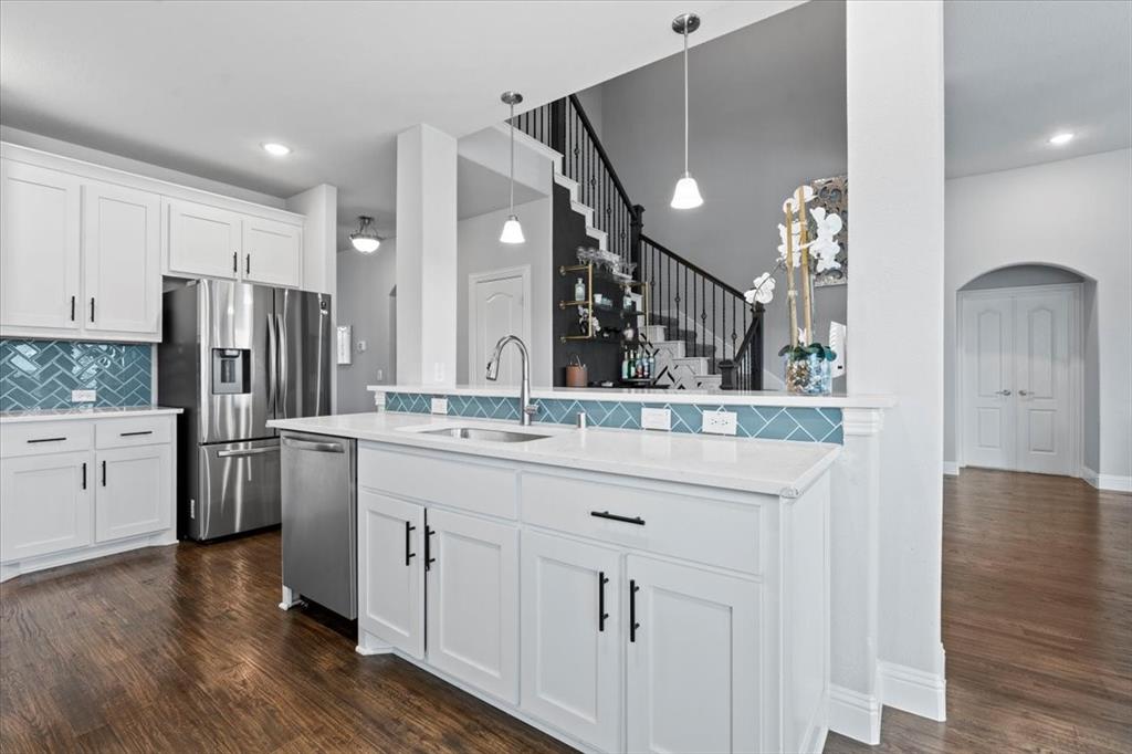 620 Shadow Trail Frisco, TX 75033 - Photo 5 of 36 Modern kitchen featuring white shaker cabinetry, stainless steel appliances, a herringbone tile backsplash, and a central island with a sink