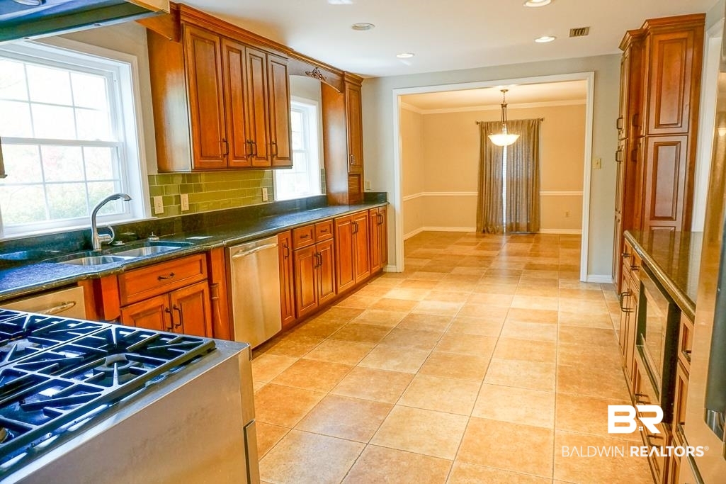 255 Suffolk Road Mobile, AL 36608 - Photo 11 of 29 Kitchen featuring crown molding, stainless steel appliances, decorative light fixtures, light tile patterned floors, and dark stone countertops