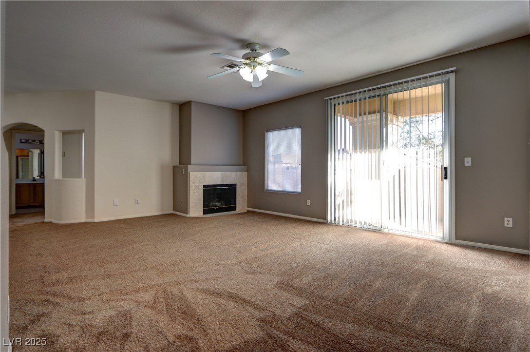 3555 Meridale Drive, Unit 2153 Las Vegas, NV 89147 - Photo 6 of 24 Unfurnished living room with carpet flooring, a tile fireplace, arched walkways, and ceiling fan