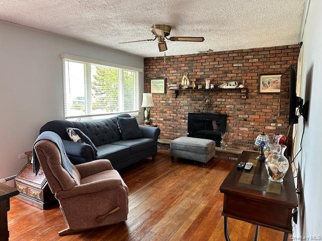4 Oakhurst Road Hampton Bays, NY 11946 - Photo 10 of 13 Living area featuring brick wall, wood-type flooring, a brick fireplace, a textured ceiling, and ceiling fan