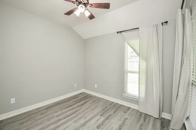 an empty room with wooden floor fan and windows