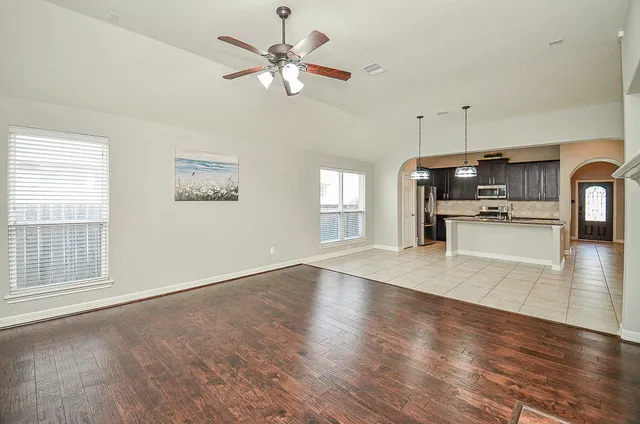 an empty room with wooden floor a ceiling fan and windows