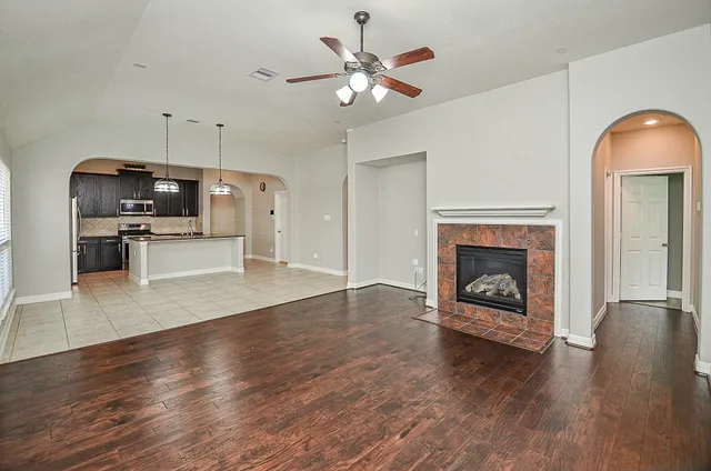 a view of a livingroom with a fireplace a ceiling fan a kitchen microwave and a refrigerator