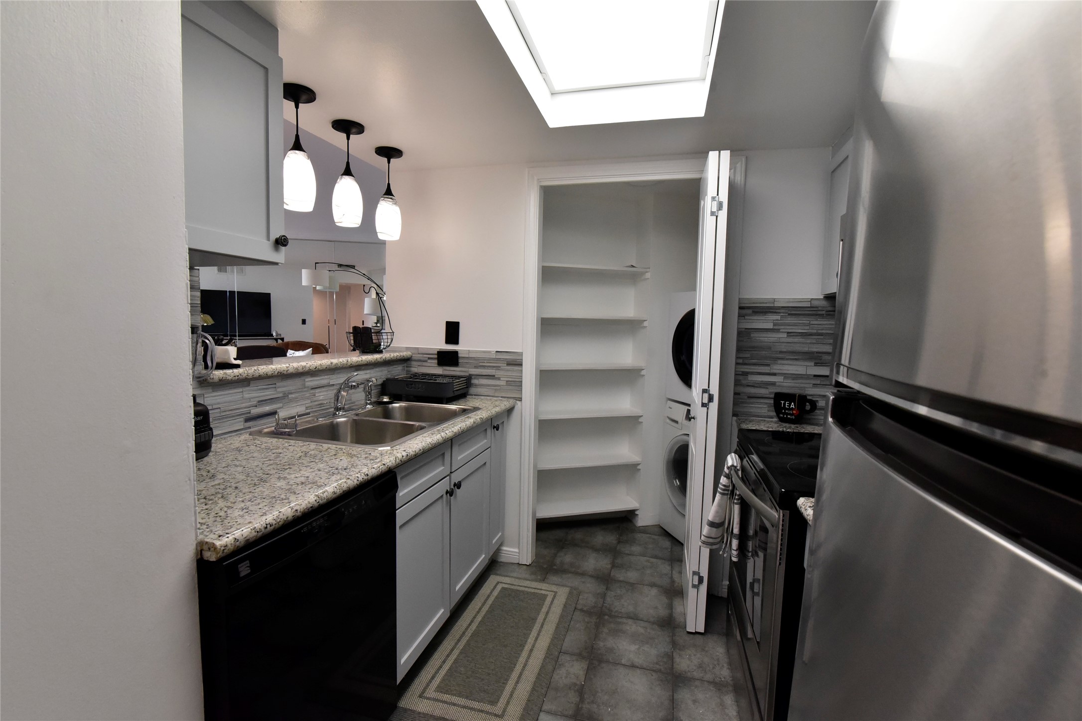 3525 Sage Road, Unit 701 Houston, TX 77056 - Photo 8 of 48 This is a modern kitchen with stainless steel appliances, granite countertops, and pendant lighting. The space features a dishwasher, a double sink, and a view into the next room through a pass-through window. A pantry with shelving as well as washer and dryer..