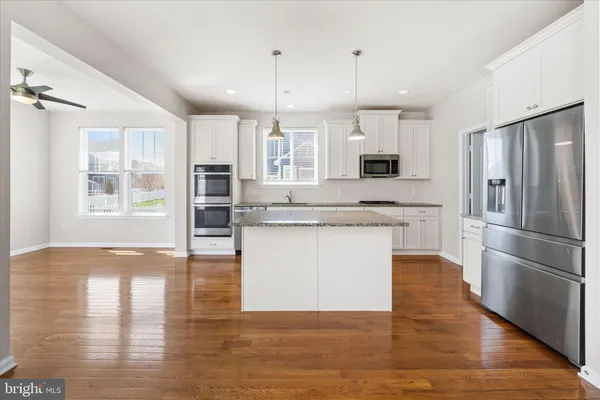a kitchen with granite countertop a refrigerator oven a sink and white cabinets