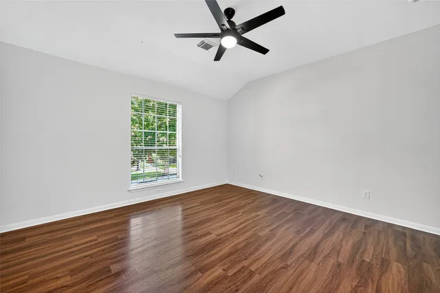an empty room with wooden floor ceiling fan and windows