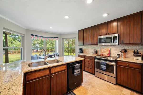 a kitchen with stainless steel appliances granite countertop wooden cabinets a sink dishwasher a stove and a refrigerator with wooden floor