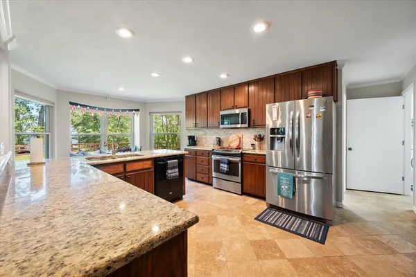 a kitchen with stainless steel appliances granite countertop a refrigerator a stove a sink a dining table and chairs