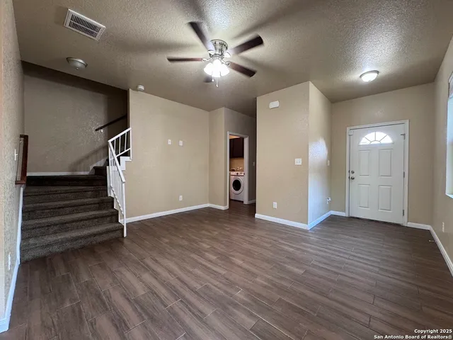 a view of an empty room with wooden floor and a ceiling fan